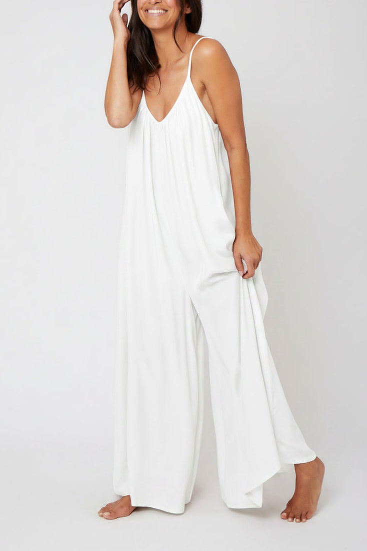 A woman modeling a white sleeveless wide-leg jumpsuit against a plain light gray studio background.